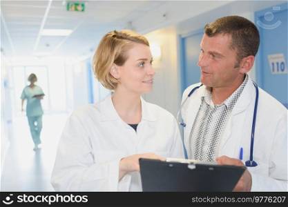 smiling doctors with clipboard walking along hospital corridor