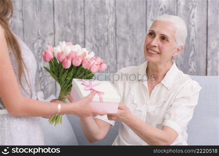 smiling elder woman receiving flower bouquet gift box front her grandchild