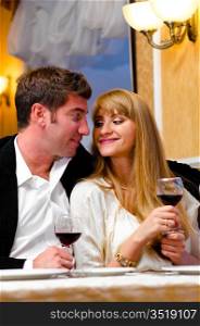 smiling embracing couple is sitting at restaurant and drinking wine