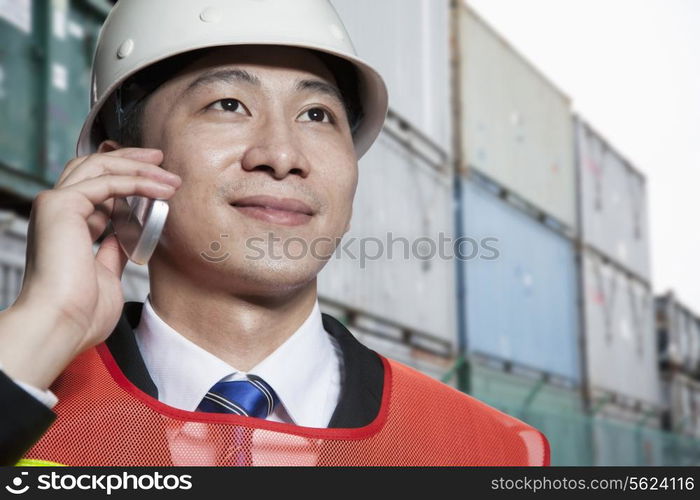 Smiling engineer in protective workwear on the phone in a shipping yard