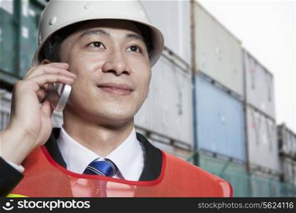 Smiling engineer in protective workwear on the phone in a shipping yard