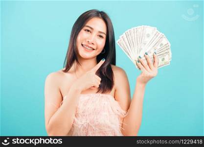 Smiling face portrait asian beautiful woman cheerful her holding and point the money on blue background, with copy space for text