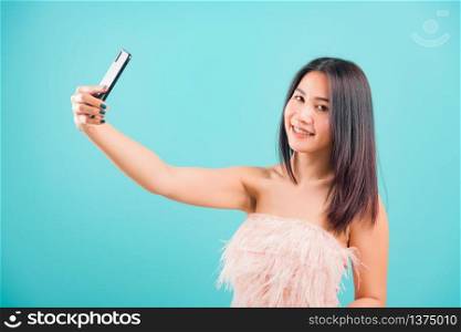 Smiling face portrait asian beautiful woman her standing making selfie photo on smartphone and her looking to camera on blue background