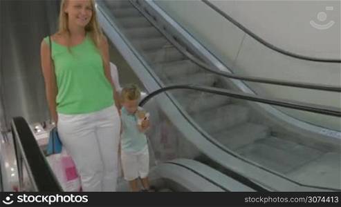 Smiling family is riding up the escalator in shopping center, man is carrying some shopping bags.