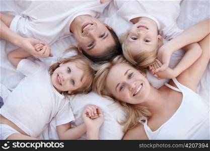 Smiling family lie on a white bed