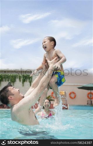 Smiling family playing in the pool, father lifting his son out of the water