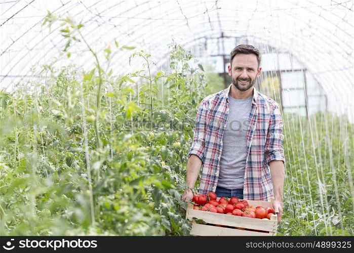 Smiling farmer carrying tomatoes in crate at farm