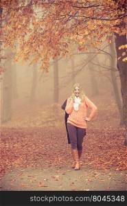 Smiling fashion blonde woman with jacket in park.. Smiling fashion woman in foggy fall autumn park. Happy attractive full length young girl holding jacket. Happiness and relax in forest.