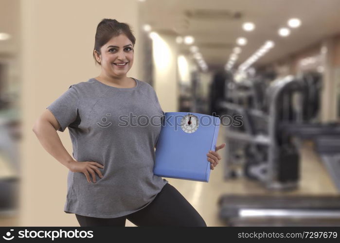Smiling fat woman in a gym holding a weight scale