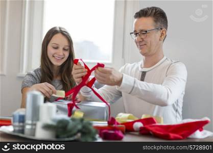 Smiling father and daughter wrapping Christmas present at home