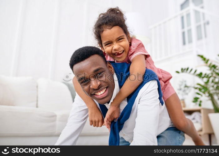 Smiling father and little daughter poses in living room. Dad and female child leisures in their house together, good relationship. Smiling father and little daughter in living room