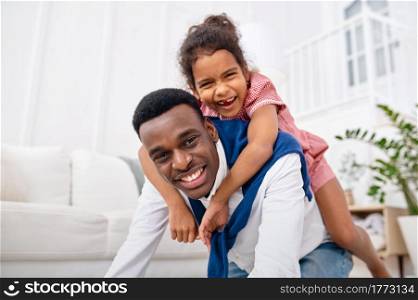 Smiling father and little daughter poses in living room. Dad and female child leisures in their house together, good relationship. Smiling father and little daughter in living room