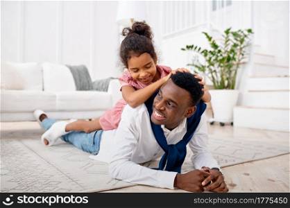Smiling father and little daughter poses in living room. Dad and female child leisures in their house together, happy relationship. Smiling father and little daughter in living room
