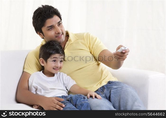 Smiling father changing channels while sitting with his son