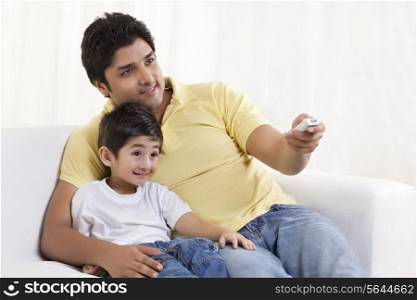 Smiling father changing channels while sitting with his son