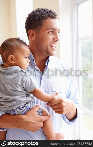 Smiling Father Standing By Window With Baby Son At Home