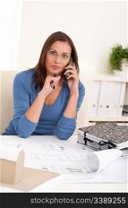 Smiling female architect holding phone and pen sitting at the office
