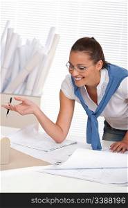 Smiling female architect watching plans and architectural model