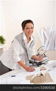 Smiling female architect with plans at the office holding glasses