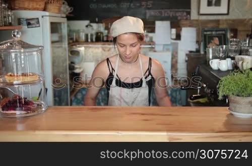 Smiling female chef putting vegetables on cutting board at the bar stand in vintage cafe