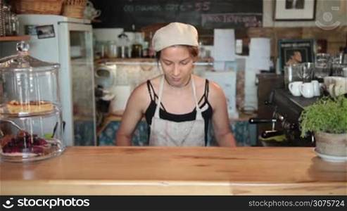 Smiling female chef putting vegetables on cutting board at the bar stand in vintage cafe