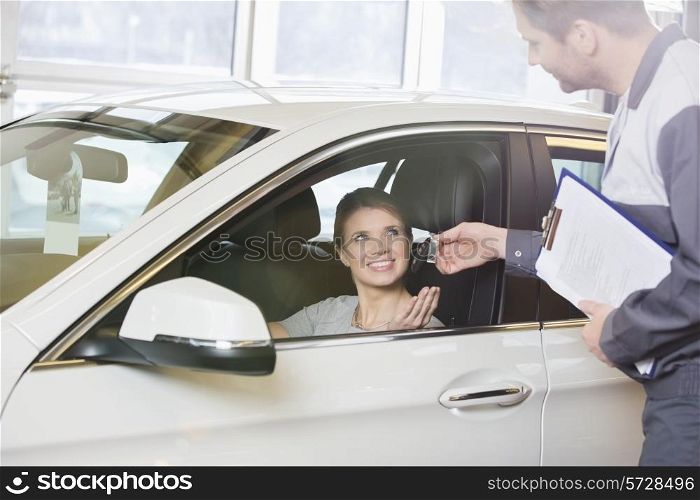 Smiling female customer receiving car key from mechanic in workshop