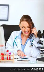 Smiling female doctor talking on phone and looking in clipboard&#xA;