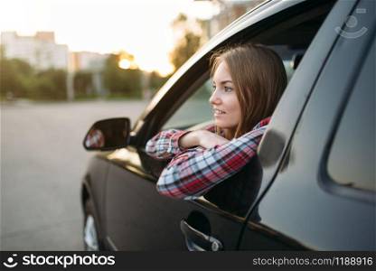 Smiling female driver beginner looks out of the car window. Woman in vehicle, driving automobile concept. Female driver beginner looks out of the car window