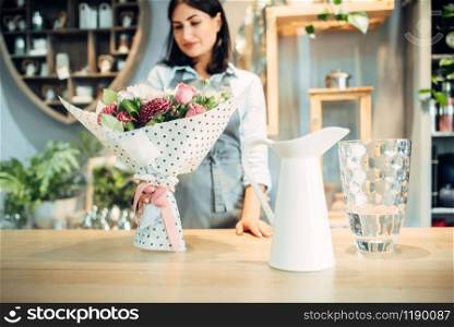 Smiling female florist looks at flower bouquet in floral shop. Floristry service, floristic business