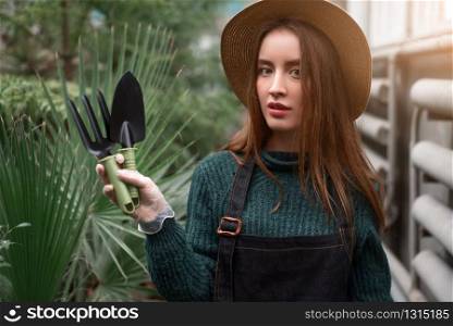 Smiling female gardener in hat and apron with garden tools in hands.. Gardener with garden tools in hands.