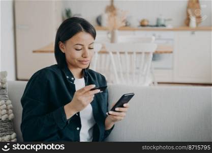 Smiling female holding bank credit card, smartphone, uses online banking service at home. Modern woman makes cashless payment, shopping on internet, using e-bank app. E-commerce, e-banking.. Smiling female holding bank credit card, smartphone, using online banking service at home. E-banking