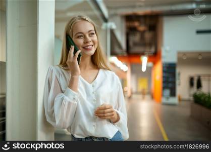 Smiling female manager talks by phone, IT office interior on background. Professional worker, planning or brainstorming. Successful employee in modern company. Smiling female manager talks by phone, IT office