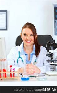 Smiling female medical doctor sitting at table in cabinet &#xA;