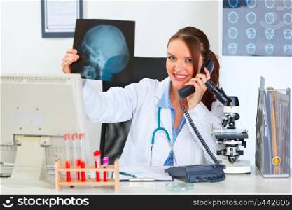 Smiling female medical doctor speaking phone and holding patients roentgen&#xA;