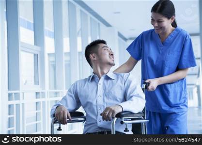 Smiling female nurse pushing and assisting patient in a wheelchair in the hospital