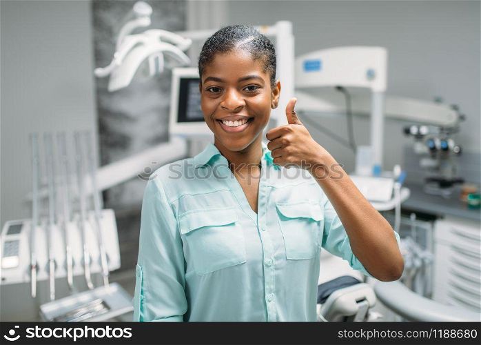 Smiling female patient shows thumbs up in dental clinic, medical equipment on background. Woman in dentistry cabinet, stomatology, teeth care. Female patient shows thumbs up in dental clinic