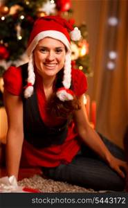 Smiling female sitting near Christmas tree &#xA;