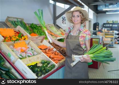 smiling female staff holding bunch of leeks in organic section
