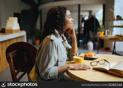 Smiling female student drinks coffee with croissants in cafe. Woman learning a subject in coffeehouse, education and food. Girl studying in a cafeteria. Student drinks coffee with croissants in cafe
