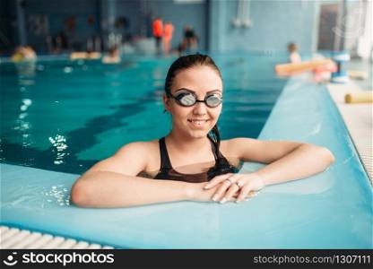 Smiling female swimmer in goggles swims in the pool. Woman in swimwear on training, swimming sport
