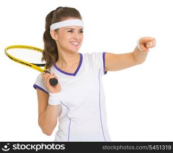Smiling female tennis player with racket pointing on copy space