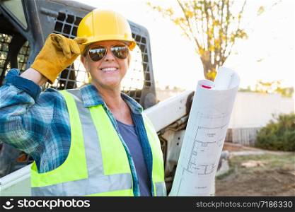 Smiling Female Worker Holding Technical Blueprints Near Small Bulldozer At Construction Site