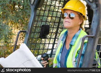 Smiling Female Worker Holding Technical Blueprints Using Small Bulldozer At Construction Site