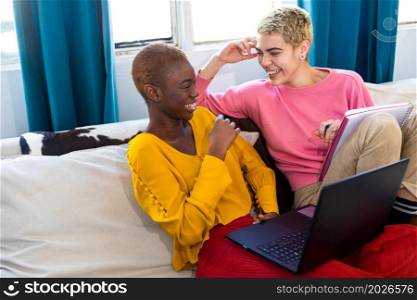 Smiling females using laptop while sitting on sofa at home. Smiling women using laptop while sitting on sofa at home