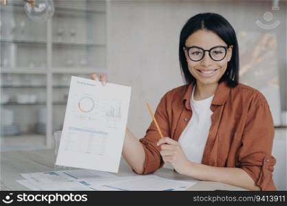 Smiling financial analyst presents company statistics, project report at desk. Happy employee showcases work report.