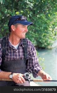 Smiling Fisherman in Cap and Waders Holding Rod and Looking to the Side
