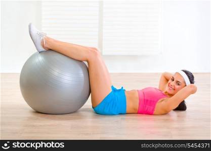 Smiling fit girl doing abdominal crunch on fitness ball at living room&#xA;