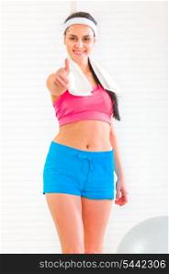 Smiling fit girl with towel around neck showing thumbs up gesture&#xA;