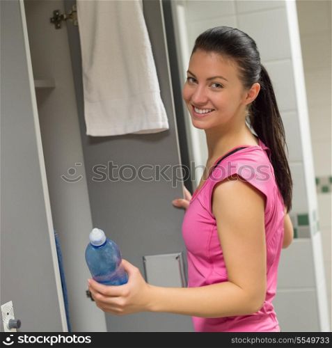 Smiling fit woman holding water bottle at gym&rsquo;s locker room