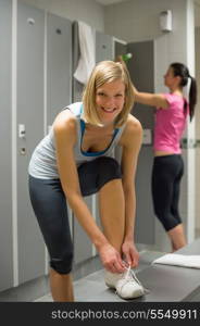 Smiling fit woman tying shoelaces at gym&rsquo;s locker room